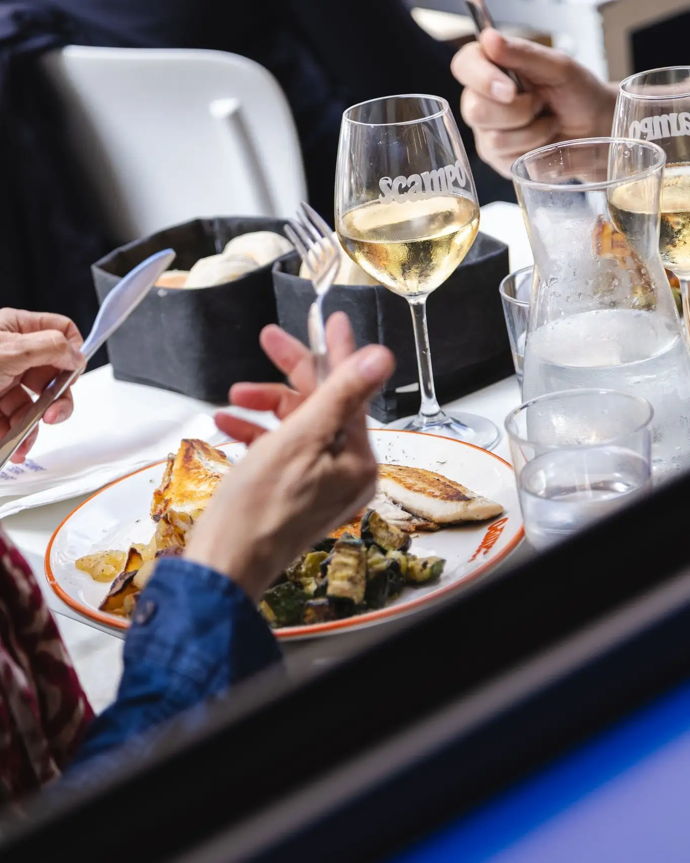 Due persone a pranzo, forchette in mano, pesce alla griglia e calici Scampo di vino bianco.